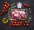 Raw pork steak with spices, butter, cherry tomatoes on a branch on wooden rustic background top view close up Royalty Free Stock Photo