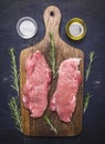 Raw pork steak on vintage cutting board rosemary, oil salt wooden rustic background top view close up