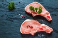 Raw pork steaks, crude cutlets with bones and fresh parsley on black stone background