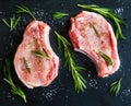 Raw pork steaks with rosemary on black stone background. Top view