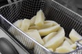 Raw potatoes, cut and chipped, in a mesh basket ready to be cooked in a deep fat fryer appliance. Royalty Free Stock Photo