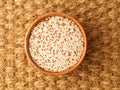 Raw Quinoa in wooden bowl, superfood. Brown sisal mat background, top view.