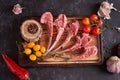 Raw rack of a calf on a cutting board with multi-colored peppercorns, red chili peppers, garlic, yellow and red tomatoes o