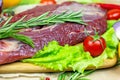 Raw red beef meat with green rosemary and fresh vegetables on light wooden cutting board background. Royalty Free Stock Photo