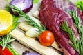 Raw red beef meat with green rosemary and fresh vegetables on light wooden cutting board background. Royalty Free Stock Photo