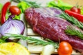 Raw red beef meat with green rosemary and fresh vegetables on light wooden cutting board background. Royalty Free Stock Photo