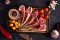 Raw rib of a calf on a cutting board with multi-colored peppercorns, red chili peppers, garlic, yellow and red tomatoes
