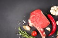 Raw ribeye beef steaks with seasonings and vegetables over dark concrete background with copy space Royalty Free Stock Photo