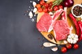 Raw ribeye beef steaks with seasonings and vegetables over dark concrete background with copy space for text Royalty Free Stock Photo