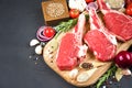 Raw ribeye beef steaks with seasonings and vegetables on wooden cutting board over dark concrete background Royalty Free Stock Photo