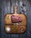 Raw ribeye steak on a cutting board with a fork, with rosemary salt and pepper on rustic wooden background, top view Royalty Free Stock Photo