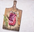Raw ribeye steak on a cutting board with a vintage meat fork and a sprig of rosemary on white wooden rustic background Royalty Free Stock Photo