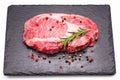 Raw ribeye steak with pepper corns and rosemary on graphite serving board isolated on white background