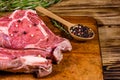 Raw ribeye steak, wooden spoon with spices and rosemary on a cutting board