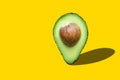 Raw ripe halved avocado with pit imitating map pointer with drop shadow on yellow background. Creative food poster banner