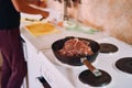 Raw roast beef is stewed in a frying pan on a stove near a cook cutting vegetables