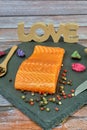 Raw salmon fillet with wooden love word, garnished with fresh herbs and spices