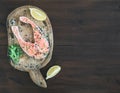 Raw salmon steak with fresh herbs, lemon and spices on rustic wooden board over a dark woog background with a copy space Royalty Free Stock Photo