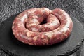 raw sausage in a round shape for grilling or roasting on a black stone background