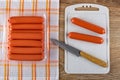 Sausages in shell in pack on napkin, two sausages and knife on cutting board on wooden table. Top view Royalty Free Stock Photo