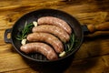 Raw sausages ready for preparation with rosemary, garlic and spices in cast iron grill frying pan on wooden table Royalty Free Stock Photo