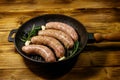 Raw sausages ready for preparation with rosemary, garlic and spices in cast iron grill frying pan on wooden table Royalty Free Stock Photo