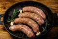 Raw sausages ready for preparation with rosemary, garlic and spices in cast iron grill frying pan on wooden table Royalty Free Stock Photo