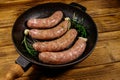 Raw sausages ready for preparation with rosemary, garlic and spices in cast iron grill frying pan on wooden table Royalty Free Stock Photo