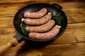 Raw sausages ready for preparation with rosemary, garlic and spices in cast iron grill frying pan on wooden table Royalty Free Stock Photo