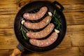 Raw sausages ready for preparation with rosemary, garlic and spices in cast iron grill frying pan on wooden table. Top view Royalty Free Stock Photo