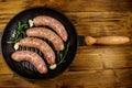 Raw sausages ready for preparation with rosemary, garlic and spices in cast iron grill frying pan on wooden table. Top view Royalty Free Stock Photo