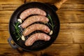 Raw sausages ready for preparation with rosemary, garlic and spices in cast iron grill frying pan on wooden table. Top view Royalty Free Stock Photo