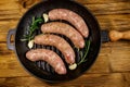 Raw sausages ready for preparation with rosemary, garlic and spices in cast iron grill frying pan on wooden table. Top view Royalty Free Stock Photo