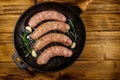 Raw sausages ready for preparation with rosemary, garlic and spices in cast iron grill frying pan on wooden table. Top view Royalty Free Stock Photo