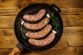 Raw sausages ready for preparation with rosemary, garlic and spices in cast iron grill frying pan on wooden table. Top view Royalty Free Stock Photo