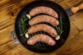 Raw sausages ready for preparation with rosemary, garlic and spices in cast iron grill frying pan on wooden table. Top view Royalty Free Stock Photo