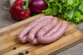 Raw sausages with vegetables on wooden cutting board Royalty Free Stock Photo