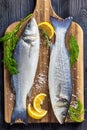 Raw sea bass fish uncooked served on a wooden board with sea salt, dill, lemon on a black wooden table, top view, close-up