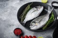 Raw sea bream or dorado raw fish on grill pan with ingredients on grey white textured background, side view space for text