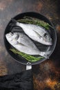 Raw sea bream or dorado raw fish on grill pan with ingredients on old metall dark background, top view