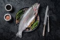 Raw Sea trout, fresh fish on a plate with herbs. Black background. Top view