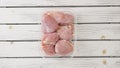 Raw skinless boneless chicken thighs in plastic container close-up on white wooden board, copy space