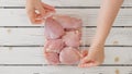 Raw skinless boneless chicken thighs in plastic container close-up on white wooden board in woman's hands