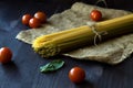 Raw spaghetti, red cherry tomatoes and green leaves with sackcloth on a wooden table Royalty Free Stock Photo