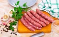 Raw longaniza on wooden board with knife, garlic, peppercorns and parsley