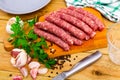 Raw longaniza on wooden board with knife, garlic, peppercorns and parsley