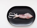 Raw squid or cuttlefish on black oval plate isolated on white background