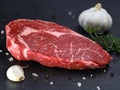 Raw Steak Ribeye with garlic and spices on black slate stone background, side view of a marbled fresh beef steak Royalty Free Stock Photo