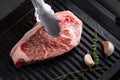 Raw Striploin steak is placed with tongs on a grill Royalty Free Stock Photo