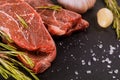 Raw striploin steak with rosemary and garlic, salt and pepper over stone table Royalty Free Stock Photo